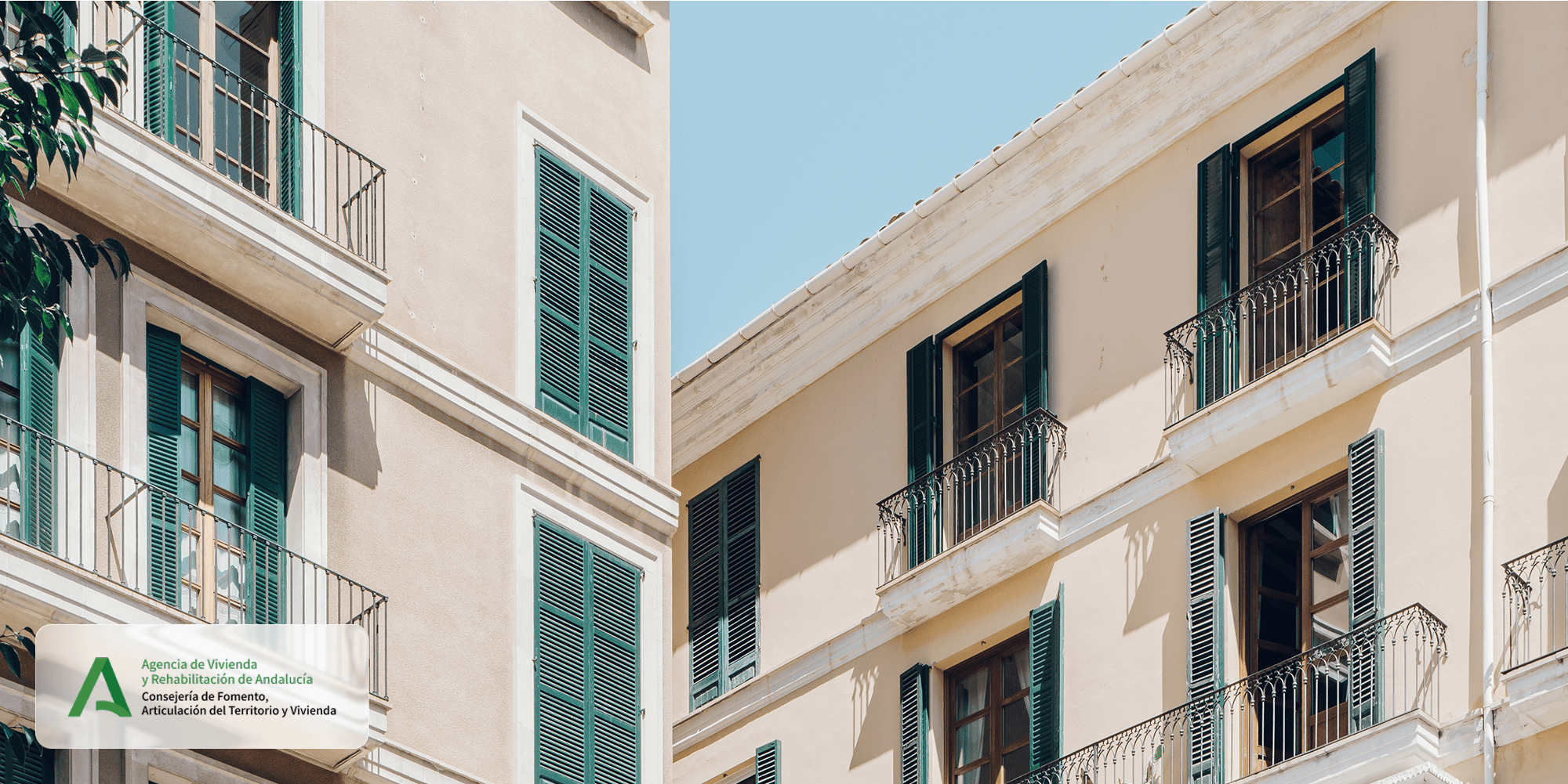 Fachada de un edificio residencial andaluz con balcones y contraventanas verdes, con el logotipo de AVRA
